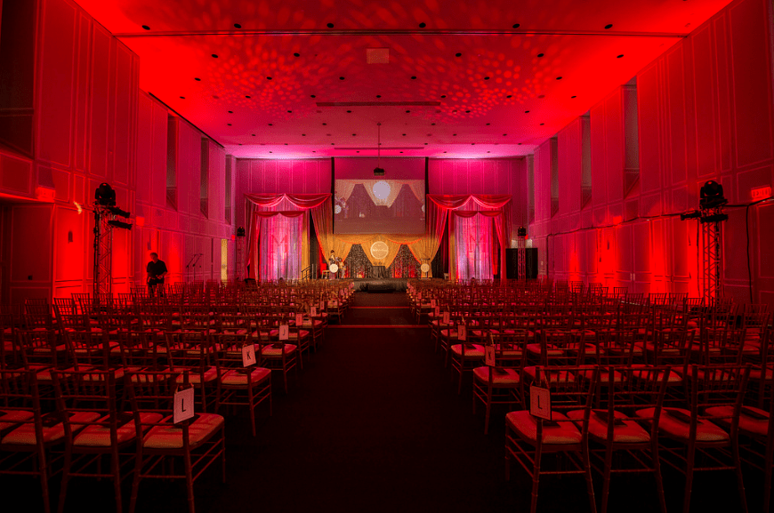 Red lite room with chairs in theater rows on either side of aisle leading to stage