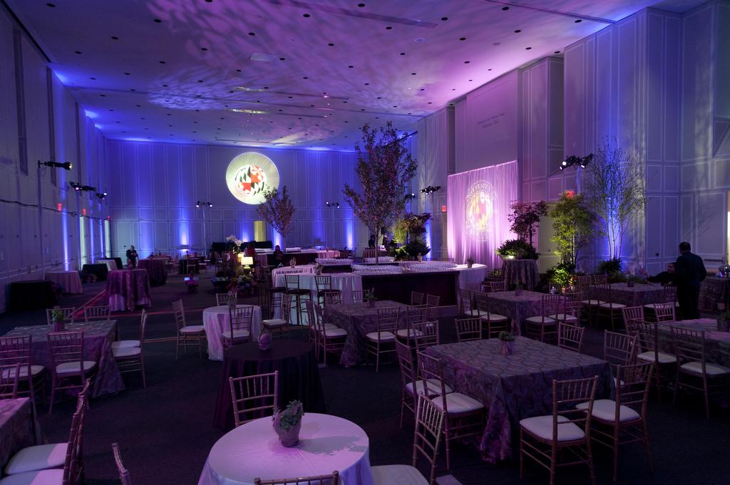 Full ballroom lit with purple and blue accent lights set with white and grey draped tables. 