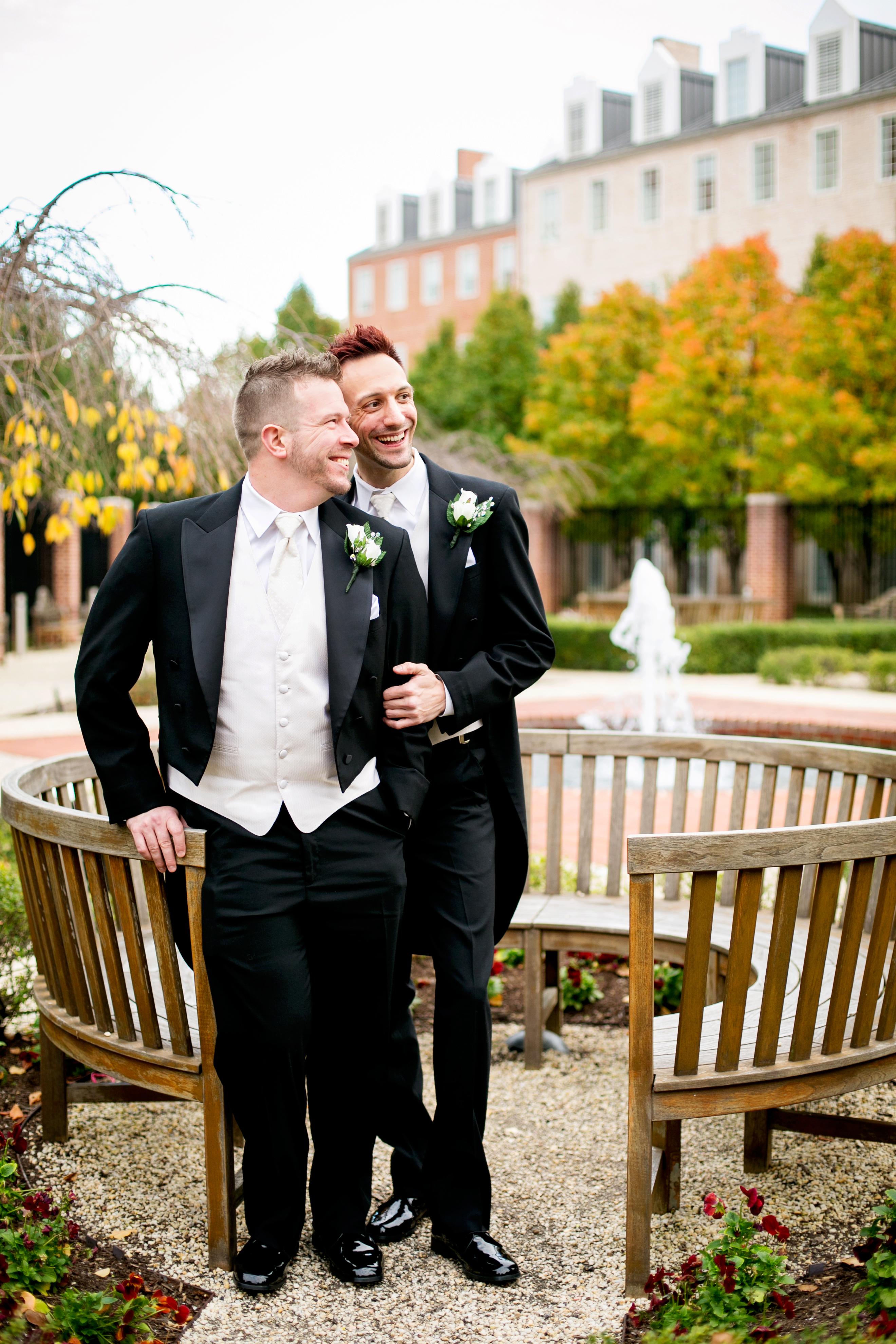 Groom and Groom in front of bench with fountain behind in garden