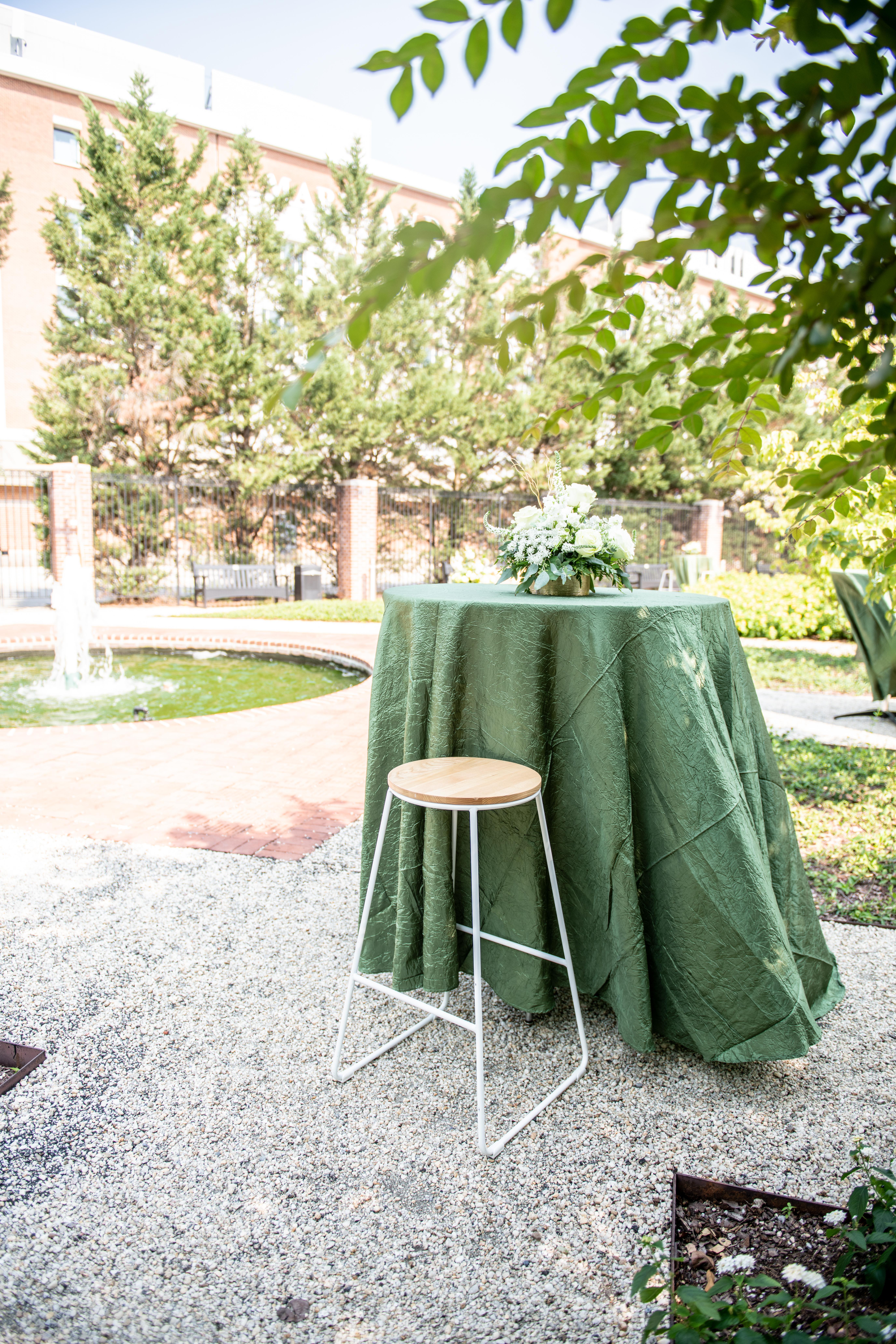 High top table with green linen in garden with fountain in background